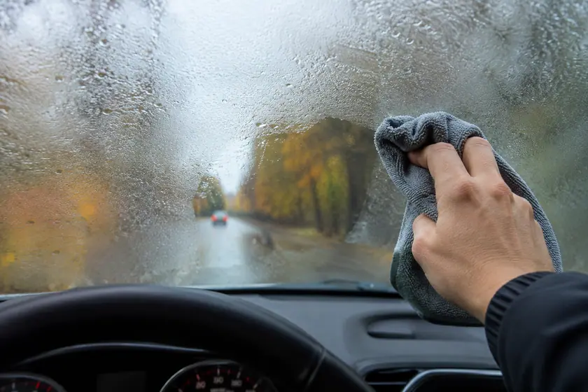 Conducteur essuyant la buée à l'intérieur du pare-brise avec un chiffon microfibre par temps de pluie