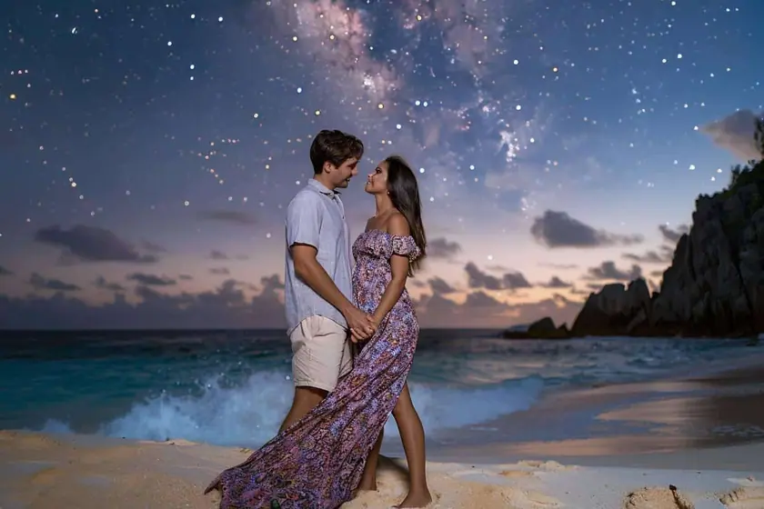 Couple assis sur une plage de sable clair sous un ciel constellé, blocs de granit en arrière-plan